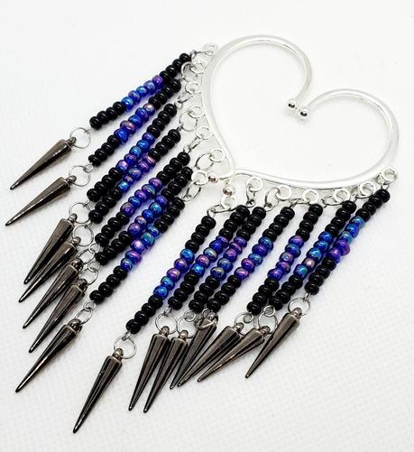 a pair of silver ear cuffs made by kiamichi. they are arranged in a heart shape. from each cuff hangs beaded wire threads starting and ending with black beads with iridescent blue and purple beads in the center. at the end of each thread hands a shiny dark gray conical spike