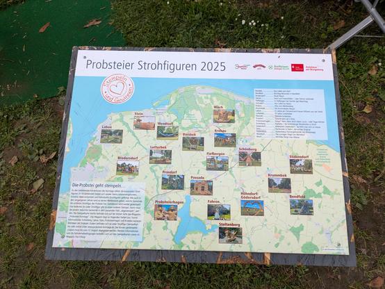 Foto: Infotafel mit einer OSM-Landkarte von der Probstei, nordöstlich von Kiel. Verstreut auf der Karte sind Fotos der jeweiligen Stroh-Skulpturen, die man in den mitmachenden Dörfern bestaunen kann.