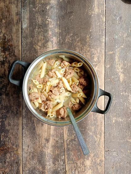 Soup with soy chunks and pasta. In a pot on a grungy wooden table.