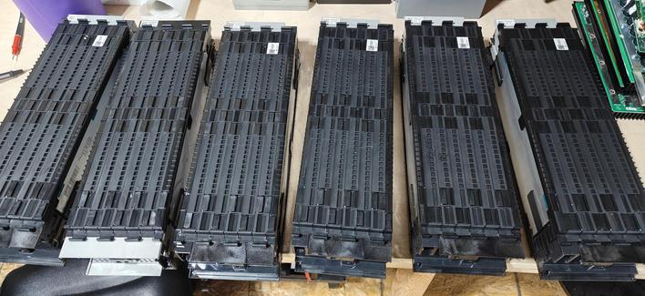 The images display LG battery cell packs, specifically designed for applications like energy storage systems (ESS).

**Key Observations:**

* **Form Factor:** The packs are long and rectangular, with a robust black casing that has a ribbed or finned texture on the sides. This design suggests an emphasis on passive cooling and efficient use of space, characteristic of prismatic battery cells that are designed for compact packaging.
* **Internal Structure: ** One pack is oriented to show a large, flat, silver-colored surface. This is a protective layer covering the individual battery cells within the module.
* **Labels and Barcodes:** On the visible silver surface, there are clear labels with text and barcodes, indicating they are mass-produced industrial components for tracking and identification.
* **Quantity:** The first image shows six identical units, suggesting they are typically deployed in multiples for scalable energy storage solutions.
* **Potential Use Cases:** Given their size and appearance, these are not small consumer batteries. They are consistent with LG's offerings in the ESS market, which includes residential and grid-scale energy storage, as well as backup power solutions for data centers and other critical infrastructure. Some LG battery modules, like the LG Chem RESU series, are designed for such applications, featuring high capacity and robust construction.