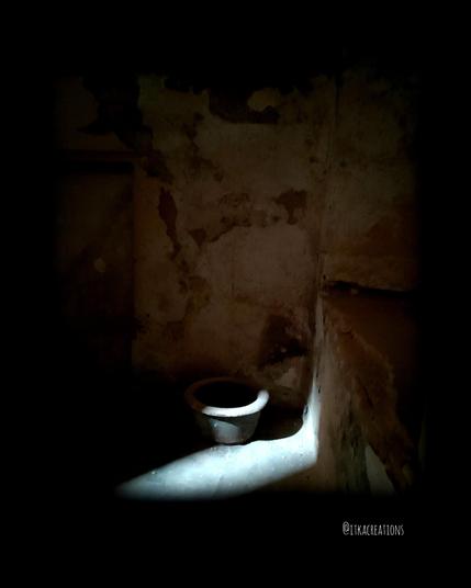 Coin d'une pièce en pierre abandonnée. Ambiance très sombre. Clair obscur. Un rais de lumière permet de découvrir... un pot de chambre.