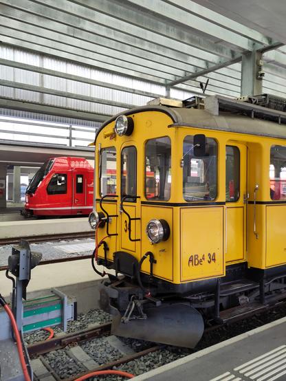 Foto. Ein gelber und ein roter Zug im Bahnhof.