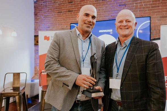 Two men stand with one holding an award