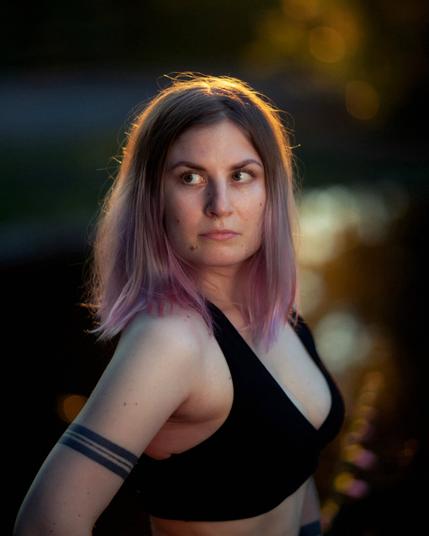 A finnish woman posing in front of a blurry pond on a summer evening