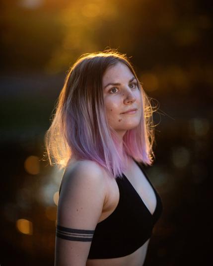 A finnish woman posing in front of a blurry pond on a summer evening