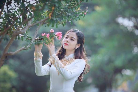 A woman looking at a pink flower.