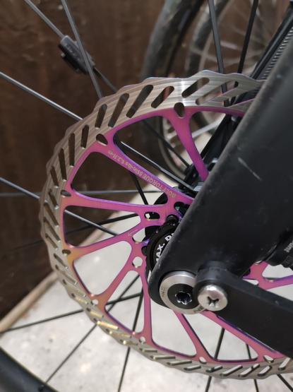 Eine lilane Bremsscheibe an einem Fahrrad. Da, wo der Bremsbelag "bremst" ist die Farbschicht abgeschliffen.