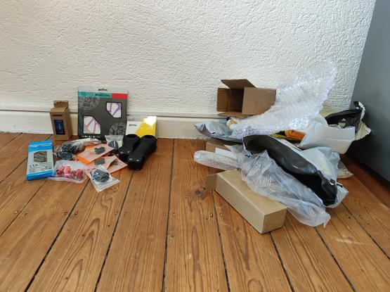 Links diverse Kleinteile auf dem Boden. Rechts der dazugehörige Verpackungsmüll. Der rechte Haufen ist deutlich größer.