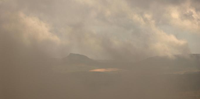 A mostly cloudy photo with just a glimpse of the view of a distant hill through the swirling mists that have engulfed the photographer