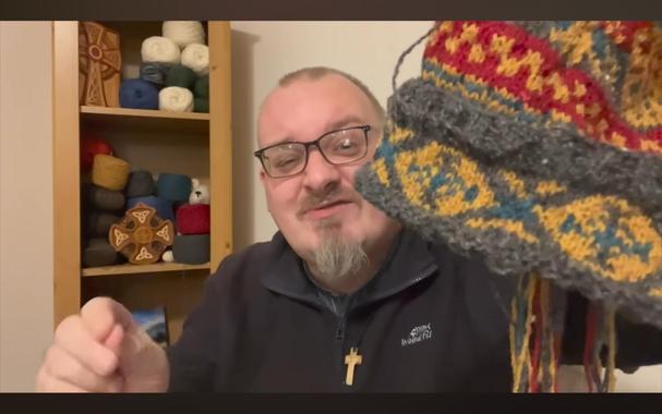 Andrew, a white dude,holding up a multi-colored knitted cap