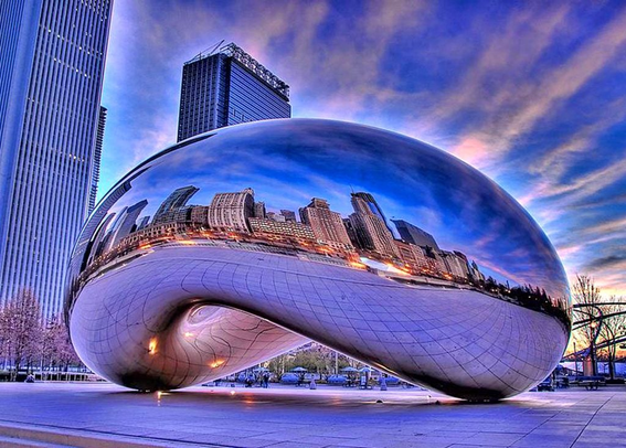 Image of Anish Kapoor's famous Cloud Gate sculpture, which is commonly known as The Bean because it resembles a coffee bean, but with a reflective surface. In the surface, you can see the reflection of tall buildings.