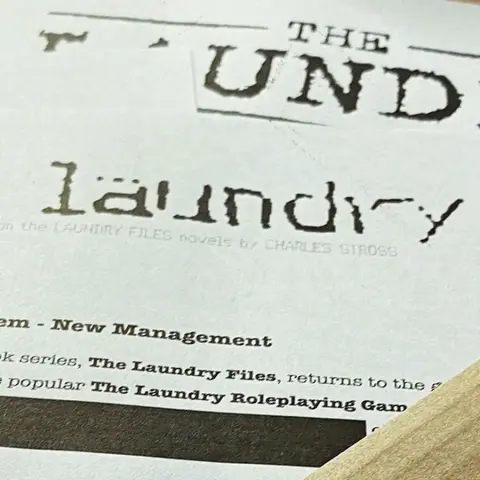 A close-up view of a printed document featuring the title "THE LAUNDRY" prominently displayed at the top, with a distressed font style. Below the title, the text indicates that it is based on the "LAUNDRY FILES" novels by Charles Stross, and mentions "System - New Management." The document appears to be part of promotional material for the latest edition of the Laundry RPG.