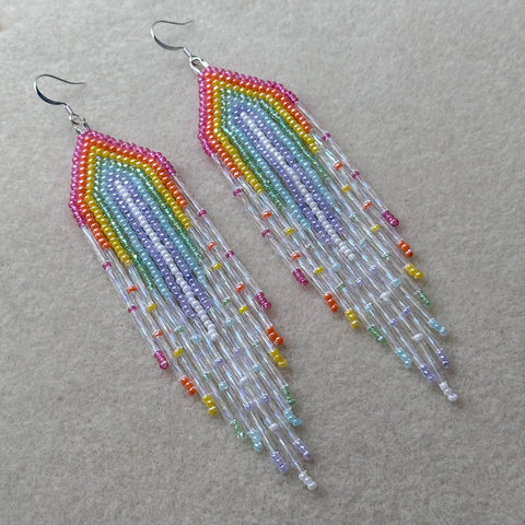 A pair of rainbow beaded fringe earrings on a bead mat
