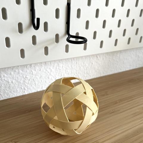 3d printed ribbon ball out of beige PLA filament at the desk in front of a skadis wall