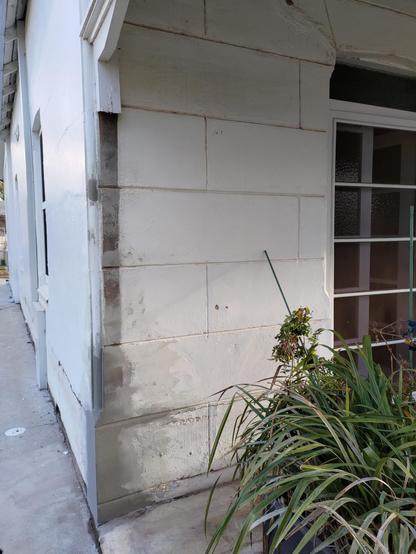 Front verandah showing rendered repairs to the concrete wall near glass french doors & potted plants