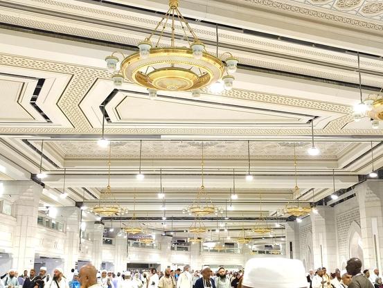 This is inside Masjid-Al-Haram (The Grand Mosque) in Saudi Arabia. It looks like a white place. Many people are walking around. There are many lights and beautiful decorative items. Everything looks grand and luxurious. The photo was taken during night time. The atmosphere was great.