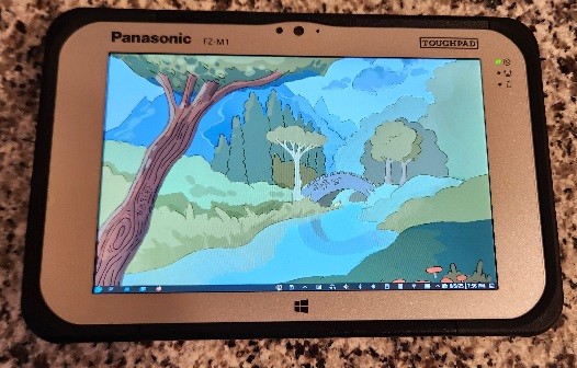 Panasonic Toughpad FZ-M1 7" tablet. It's silver. It has huge bezels. You can see Fedora Kenoite 42 on the screen, with default wallpaper.