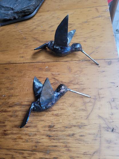 2 colibris grandeurs nature en acier recyclés sont déposés sur une meuble en bois usé.