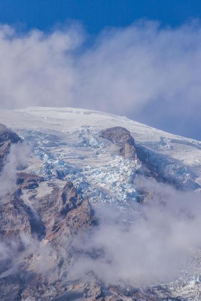 Close-up of glacier on a mountain, partially covered by clouds and rocky terrain.