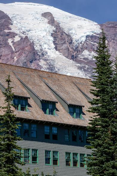 Wooden lodge with green windows in the foreground, snow-capped mountain visible behind it.