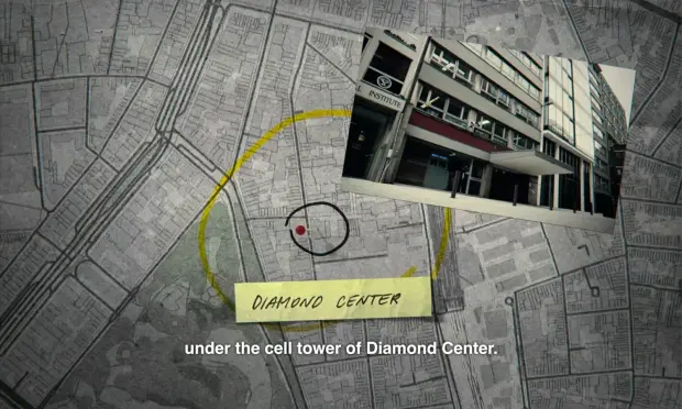 Frame from the 2025 documentary Stolen: Heist of the Century showing a desaturated basemap of central Antwerp, Belgium, centered around the diamond district with a red pin at the center labeled “Diamond Center” and with an accompanying photo of the building’s faade. A subtitle caption says, “under the cell tower of Diamond Center.”