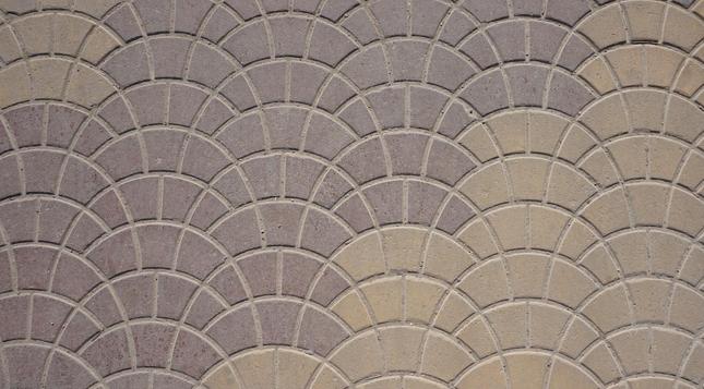 Nested arcs of pavers with curved edges. Most of the pavers are purple except a few in the top left and most in the lower right which are dun. The ends of some arcs are shared.