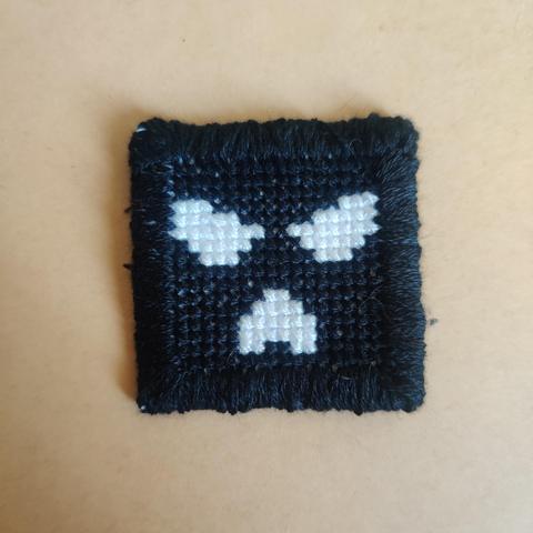 Kneecap logo patch in black and white. It looks like white eyes and a white mouth in a black balaclava.