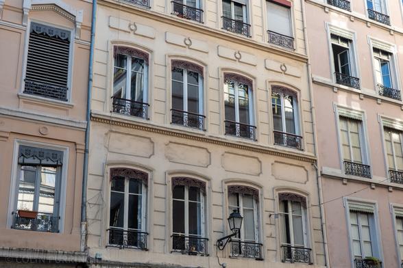 Windows on stone apartment buildings. At the top of each window there's some sort of decorative metalwork that extends down approximately 6 inches. And each window has a metal guard rail that is also decorative.