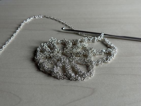 Silver chain with a crochet hook on a tabletop.