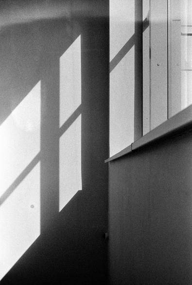 The photo features a black and white composition with a focus on the play of light and shadow. You can see how the window casts shadows on the wall. The light creates geometric shapes that give the photo an abstract and minimalist appearance.