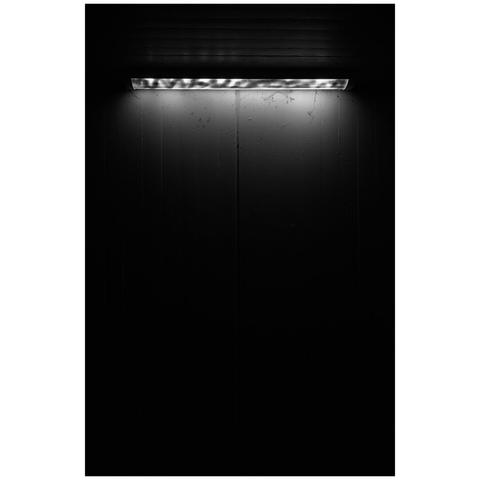 A ceiling light in front of a concrete wall. The light is quite dimm and everything quickly fades into black.