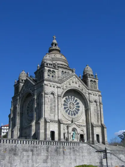 The image features a grand architectural structure that appears to be a church or a cathedral. It showcases intricate stonework, large arches, and a prominent rose window. The structure has multiple domes and towers, set against a clear blue sky, which highlights its impressive features. The overall design seems quite ornate and likely reflects a historical or religious significance.

Image Credits: Wikimedia / Usuário:jlrsousa do flickr / CC BY-SA 2.0