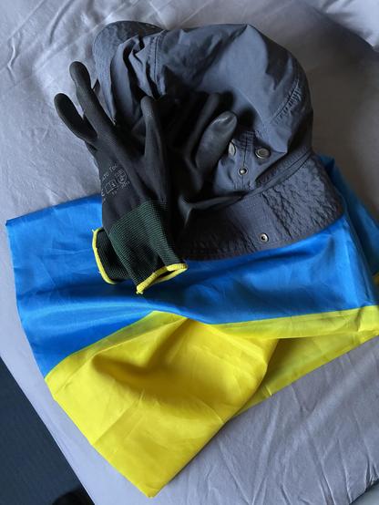 Foto einer Ukrainischen Flagge, einem Hut und Arbeitshandschuhe.