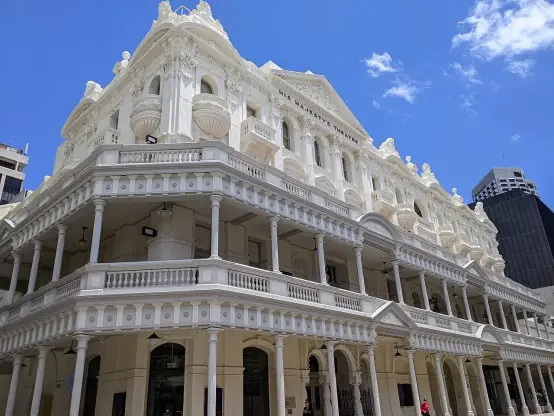 The image shows a grand, classical-style building featuring white architecture with decorative elements, balconies, and columns. The structure appears to have multiple stories and is set against a bright blue sky, indicating a sunny day. The building likely has historical significance given its ornate design.

Image Credits: Wikimedia / The Logical Positivist / CC BY-SA 4.0