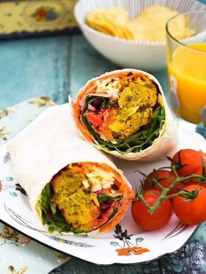 Colourful halved onion bhaji wrap on a plate with cherry tomatoes and served with orange juice.