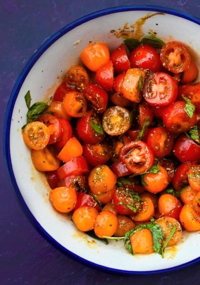 Bowl of marinated halved cherry tomatoes with fresh herbs.