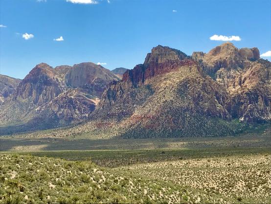 Scenic view of rugged mountain peaks under a bright blue sky, surrounded by green and brown desert vegetation.