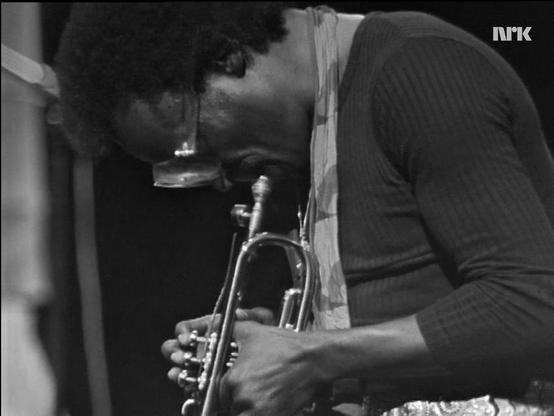 NRK b/w medium screen capture of Miles Davis hunched over his trumpet.