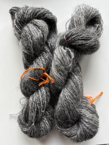 Two hanks of heathered grey yarn. They are loosely plied and have a bit of sheen and halo too.