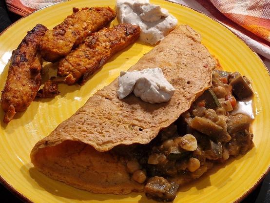Das beschriebene Essen, gefüllte Pfannkuchen, Sauce und Seitan auf gelbem Teller