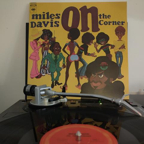LP sleeve of Miles Davis - On The Corner propped up behind a turntable which is playing the album.