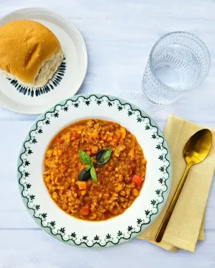 Bowl of red pepper lentil soup served with a Scottish soft morning roll and a glass of water.