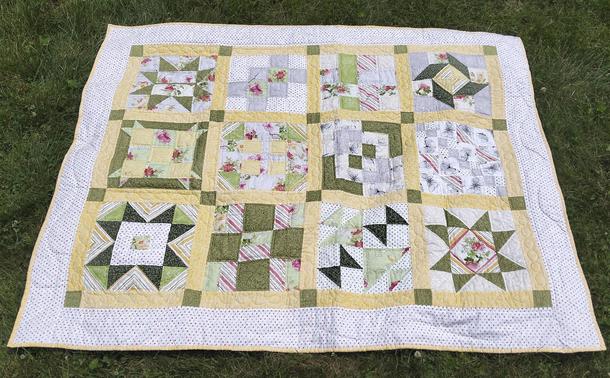 a quilt, it is a 12-box quilt, inside are unique designs in each box done with greens and yellows, separated by yellow bars and corner squares, against a light backing