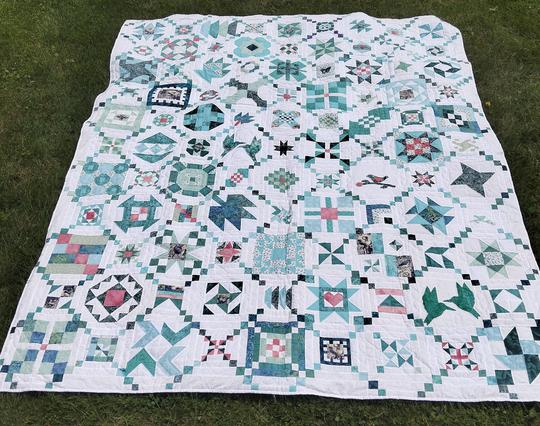 a large quilt, complex designs on it done in blues and teals and light reds , against a white backing