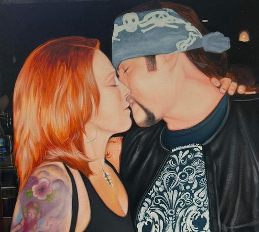 a photo of a woman with red hair kissing a man with a bandana tied around his head with skull and crossbones on it, wearing a leather jacket and black shirt with white design on it, she is in a black tank top , they are kissing each other, they are in a bar setting