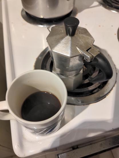 Espresso maker on stove.  A cup of espresso beside it, successfully made.
