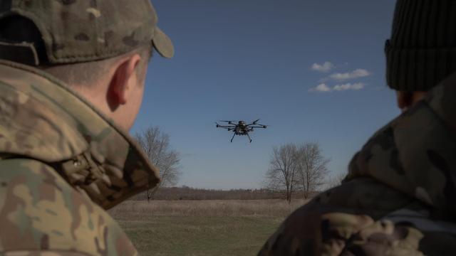 Zwei Militärangehörige beobachten eine Drohne, die über einem Feld aufsteigt.