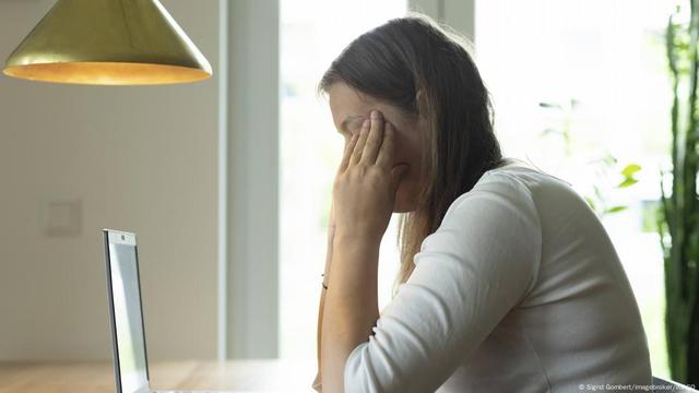 Junge Frau sitzt vor dem Laptop, Finger an die Schläfen gelegt