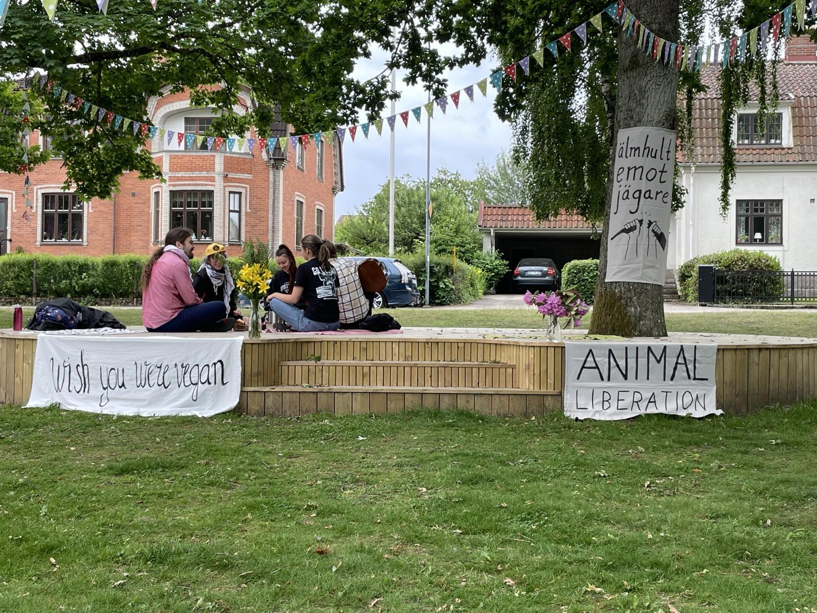 Banners saying” Wish you were vegan” , “Animal liberation”, “älmhukt emot jägare” and group of people sitting on the stage on the älmhult’s animal rights day