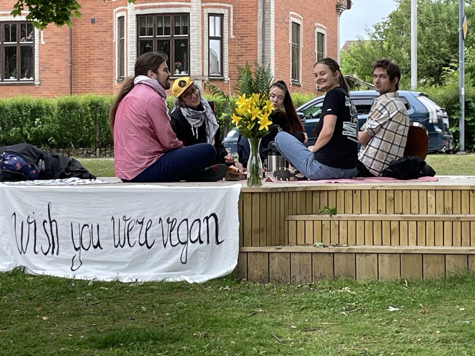 Banner saying” Wish you were vegan” and smiling group of people sitting on the stage on the älmhult’s animal rights day